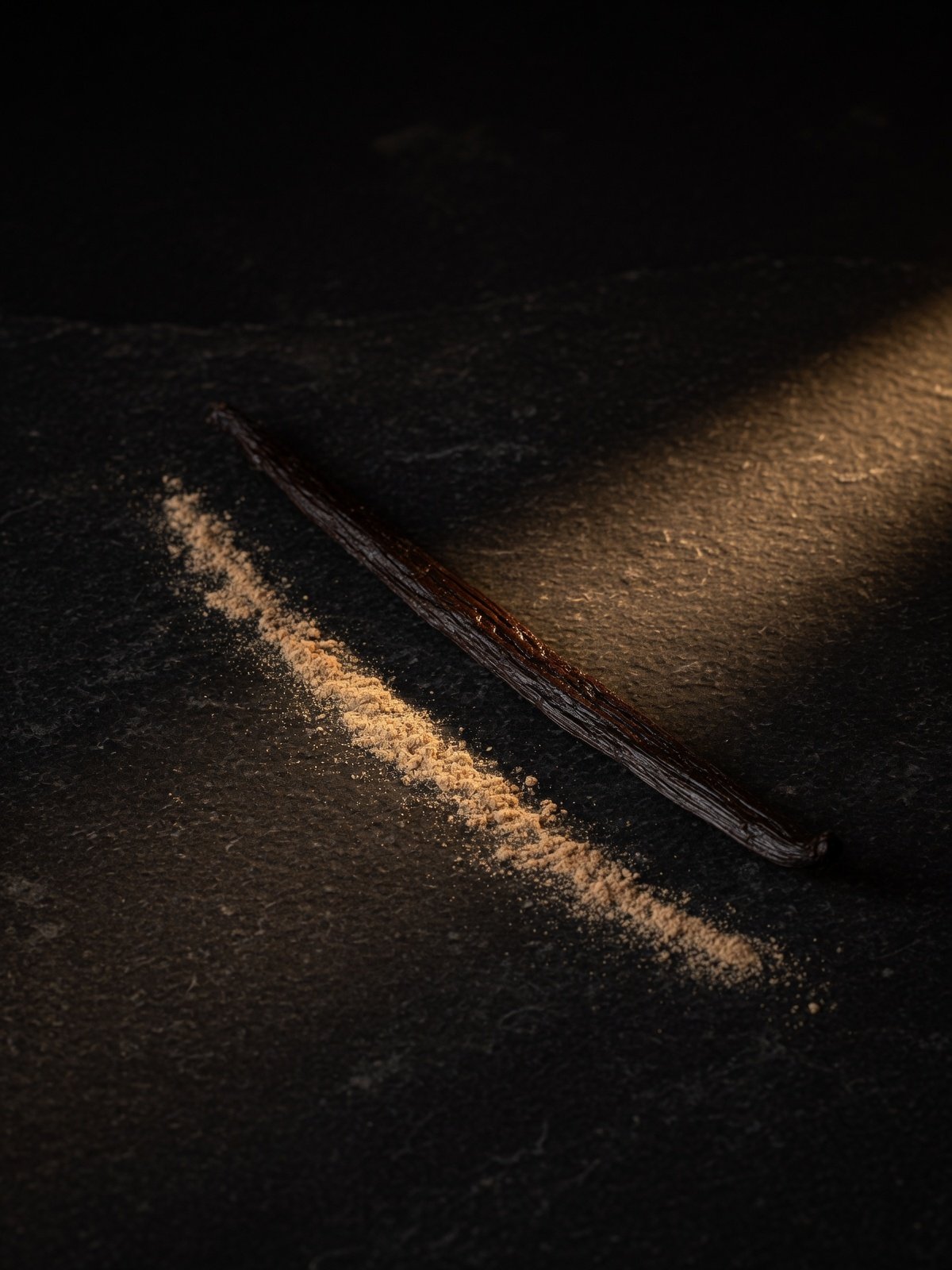 A vanilla pod with a trail of powder in low light